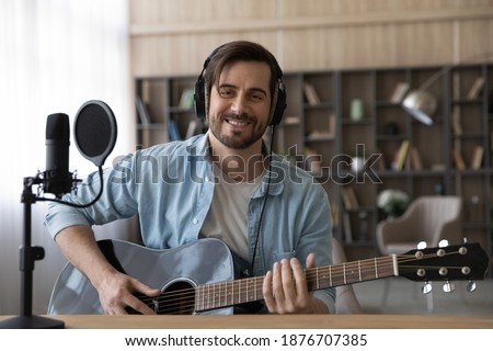 Portrait of smiling millennial Caucasian male singer or composer hold guitar record new single at home studio. Happy young 20s man artist compose song play on electric music instrument. Hobby concept. Royalty-Free Stock Photo #1876707385