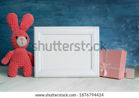 Small pink bunny sits next to gifts for children and a blank white frame for children's day and birthday greetings.copy space.Layout