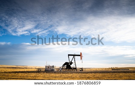 An industrial oil pump jack working on farm land under a morning sky in Rocky View County Alberta Canada. Royalty-Free Stock Photo #1876806859