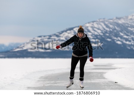 Woman skating on frozen lake in northern Canada with huge mountains in the background surrounded by snow, snow capped and glassy ice on lakes surface. 