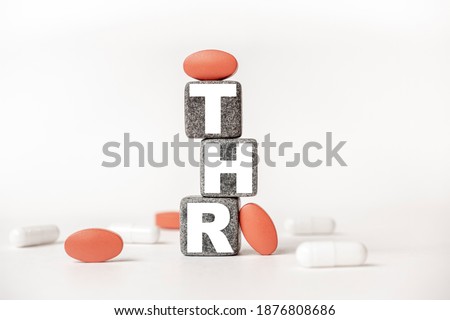 a group of white and red pills and cubes with the word THR Total hip replacement on them, white background. Concept carehealth, treatment, therapy.
