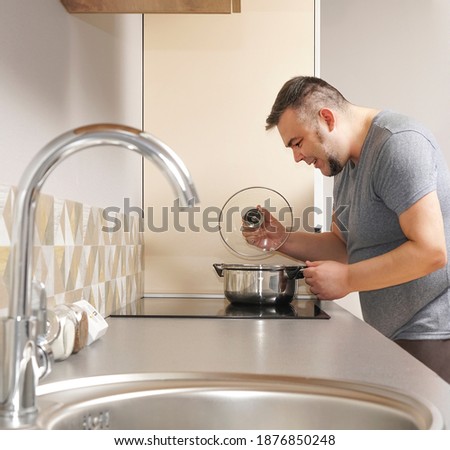 A man removes the lid from the pan -  boiling water - home cooking in quarantine. kitchen interior on background
