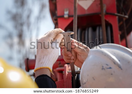 A technician is using vernier caliper to measures length of crane lifting machine part. Close-up and selective focus at center. Industrial action photo.