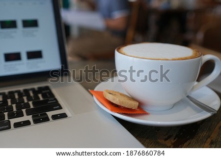 A cup of cappuccino coffee, latte coffee in a white cup with laptop on the table. Royalty high-quality free stock photo of drink cappuccino, capuchino or latte coffe with laptop for working in office