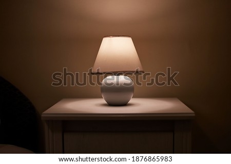 Small lamp glowing in bedroom night stand, dim room Royalty-Free Stock Photo #1876865983