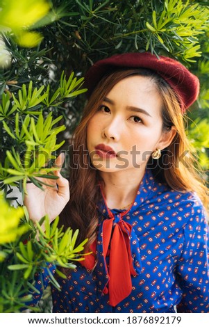 Portrait picture of wavy brunette woman in blue and red retro dress standing at the green leaf, vertical.
