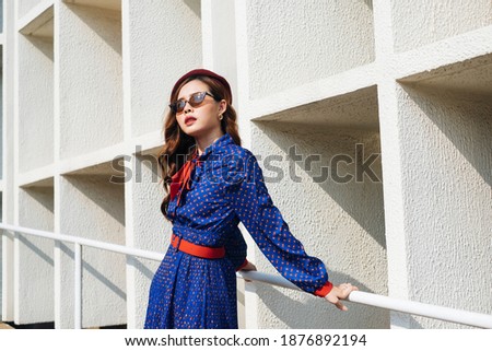 Wavy brunette woman in blue and red retro dress sitting on white handrail on the slope path with leading line.