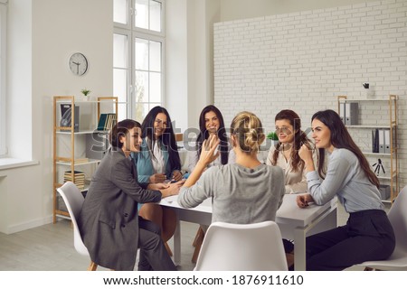 Group of young smiling businesswomen office workers or company employees sitting in circle at desk in modern loft office interior and planning projects together. Women working in company concept Royalty-Free Stock Photo #1876911610