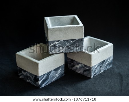 Three empty modern painted geometric concrete planters on on dark background. Cement pots, cubic shape.