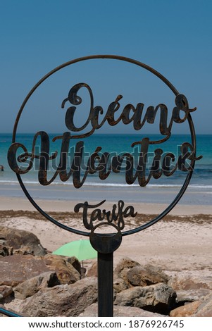 A vertical shot of a round "Oceano Atlantico Tarifa - Atlantic Ocean Tarifa" sign on the beach in Spain