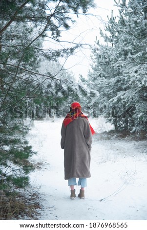 a girl in a red scarf and a long coat walks through a snow-covered forest