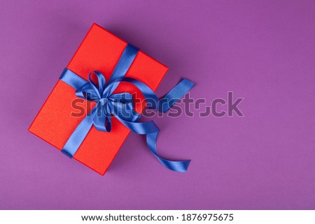 red gift or present box with blue ribbon on violet background. composition for birthday, valentine day, mother day or wedding. top view copy space 