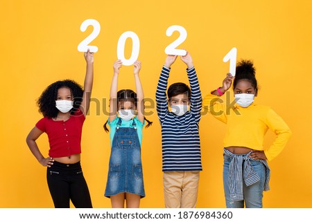 Cute mixed race children wearing medical face masks holding 2021 numbers isolated on yellow background, new year in time of pandemic concepts Royalty-Free Stock Photo #1876984360