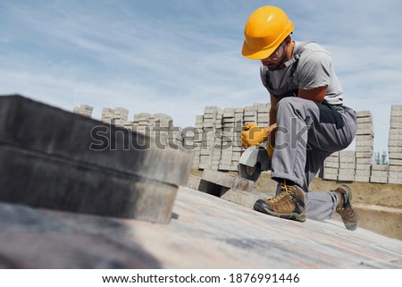 Slicing by circular saw. Male worker in yellow colored uniform have job with pavement. Royalty-Free Stock Photo #1876991446