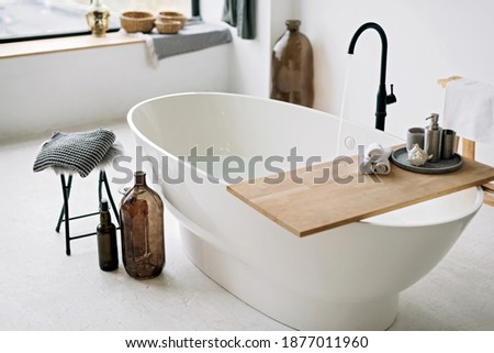 White bathtub fills with foam water in a modern apartment with stylish loft-style interior design, home decor. Spa concept, relaxation. Soft selective focus. Royalty-Free Stock Photo #1877011960
