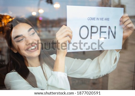 Portrait of a happy business owner hanging an open sign on the door at a cafe and smiling - food and drinks concepts. Woman at small business entrance