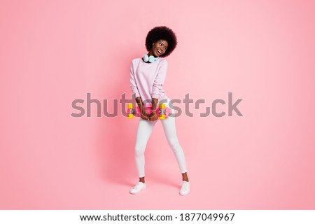 Full length body size view of pretty cheery thin wavy-haired girl carrying skate enjoying having fun isolated over pink pastel color background