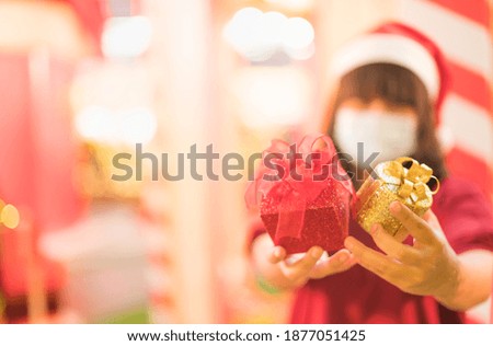 The pretty girl holding the red box with red ribbon ornament and wearing surgical mask for protect and safety for the Covid-19 coronavirus pandemic and Christmas concept.
