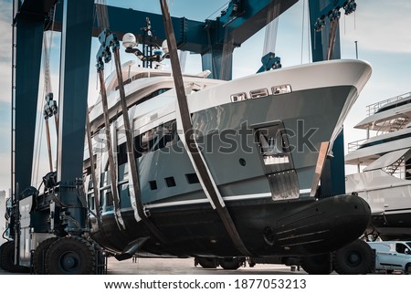Superyacht being hauled out of the water with big cranes into dry shipyard storage  Royalty-Free Stock Photo #1877053213