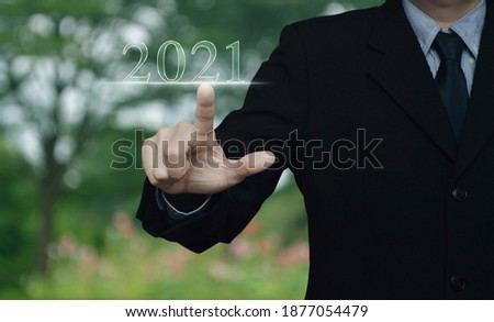 Businessman pressing 2021 text over blur flower and tree in park, Happy new year 2021 calendar cover concept