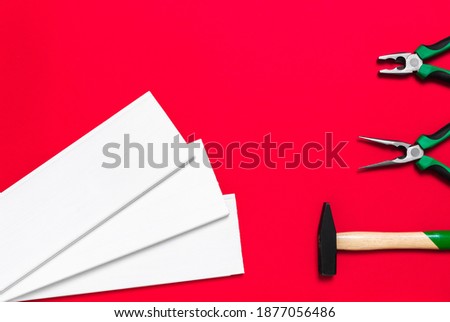 Hammer, pliers and white planks on a red background with place for text. Shop banner with construction tools, materials and instrument. New Year or Christmas holiday backdrop. Business card. Nobody.