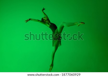 Attention. Young and graceful ballet dancer isolated on gradient green studio background in neon. Art, motion, action, flexibility, inspiration concept. Flexible ballerina, weightless jumps.