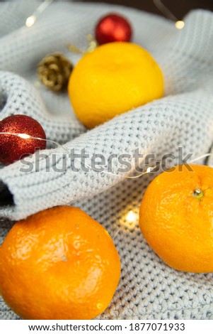 Knitted scarf, with tangerines and Christmas ornaments. Christmas decorations on a wood texture background. Christmas lights.
