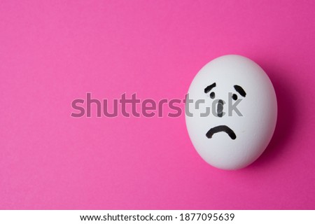 An egg with a sad face, on a pink background with copy space.