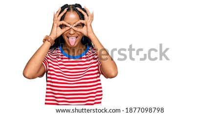 Beautiful hispanic woman wearing casual clothes doing ok gesture like binoculars sticking tongue out, eyes looking through fingers. crazy expression. 