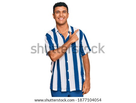 Young arab man wearing casual clothes cheerful with a smile of face pointing with hand and finger up to the side with happy and natural expression on face 