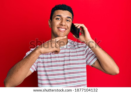 Young arab man having conversation talking on the smartphone smiling happy pointing with hand and finger 