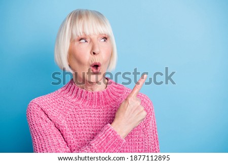 Photo portrait of impressed old woman pointing finger looking at blank space isolated on pastel blue colored background