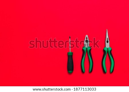 Quality green building pliers and screwdriver tools for repair a car or house on red background. Do it yourself instrument. Banner for advertising construction shop with copy space. Business card.