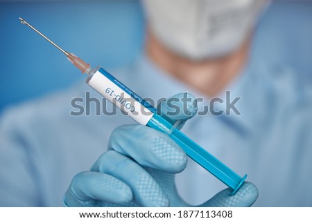 Close up of a researcher with face mask and blue gloves holding a syringe with covid-19 vaccine. Moderna vaccine. Biontech vaccine Pfizer Astrazeneca Curevac. Close up of a syringe with vaccine. Royalty-Free Stock Photo #1877113408