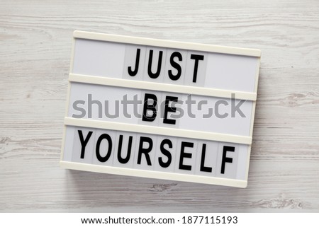 'Just be yourself' on a lightbox on a white wooden background, top view. Flat lay, overhead, from above. 
