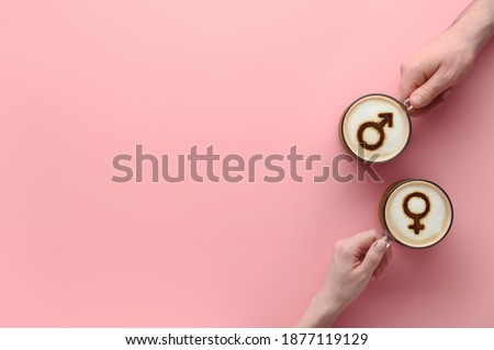Top view Hands of couple in love holding cups of coffee with symbols of venus and mars on milk foam on pastel pink background. Concept romantic date on Valentine's day. Creative flat lay, copy space