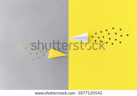 Toned in trendy yellow and grey paper planes with star shaped confetti trails flat lay. Minimalist background with copy space. Color 2021 concept. Festive and travel concept.
