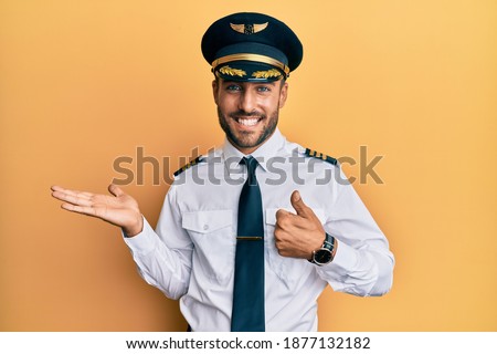 Handsome hispanic man wearing airplane pilot uniform showing palm hand and doing ok gesture with thumbs up, smiling happy and cheerful 