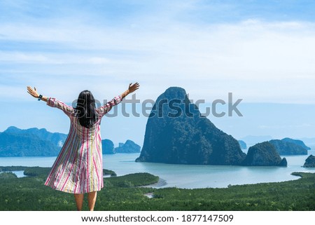 woman standing with hands up against mountain landscape on sunny summer day