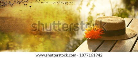 woman hat with orange flower on wood terrace in summer sunset at natural lake meadow water travel banner background