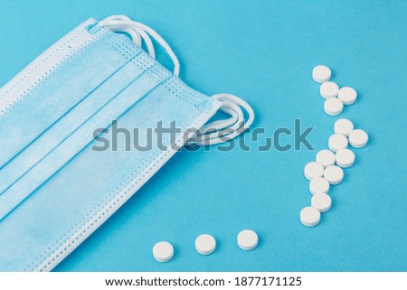 Prevent coronavirus. Medical protective mask whith white pills, isolated on blue background. Disposable surgical face mask cover mouth and nose. Healthcare, medical concept.