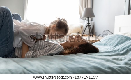 Wide banner panoramic picture of overjoyed young Caucasian mom feel playful have fun with little daughter. Happy mother play with excited small girl child, relax together in cozy bed in home bedroom.