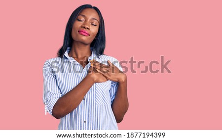 Young african american woman wearing casual clothes smiling with hands on chest with closed eyes and grateful gesture on face. health concept. 