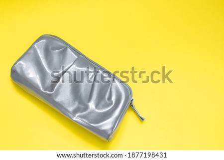 Gray shiny cosmetic bag on a yellow background. Place for your text. Trending colors of 2021.