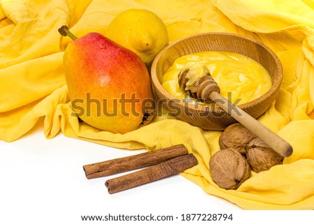 Honey in wooden plate, pear, lemon, walnuts and cinnamon sticks on yellow tablecloth. Healthy eating, dieting products