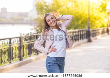 Attractive Caucasian young woman blonde in casual clothes pink jacket with pleasure poses during a walk in the park on a warm autumn day. Lifestyle, youth, beauty.