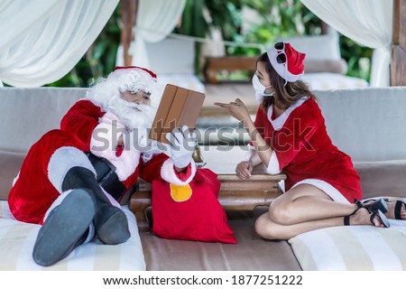 Santa Claus and his wife Mrs. Claus lying down on the tropical beach bed and using digital tablet. Christmas, holidays, technology, vacation and people concept