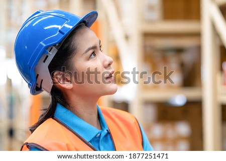 Close up woman worker standing in the automotive parts warehouse store and look on the shelf. Female engineers wear a safety helmet, vest standing in the factory. In background shelves with goods