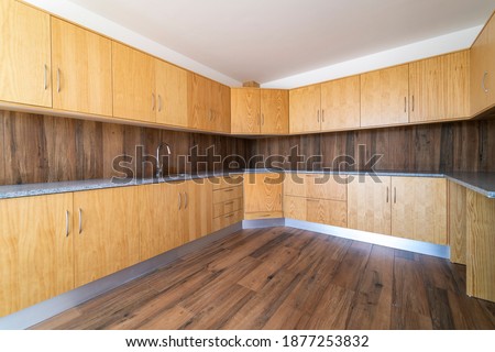Empty kitchen with dark wooden floating laminate flooring. House interior, wide dinner area or space. Newly apartment or house. Wood floor and kitchen cabinets. Real state. All in wood.