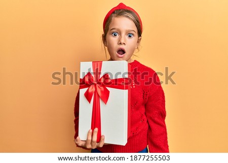 Little beautiful girl holding gift scared and amazed with open mouth for surprise, disbelief face 